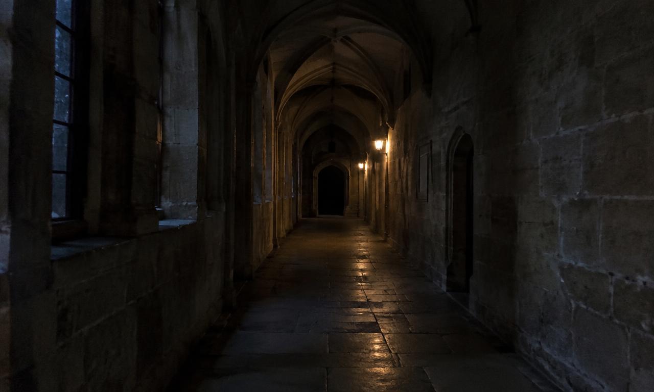 Un long couloir voûté, éclairé par une seule lampe lointaine, quand les pas se font entendre.